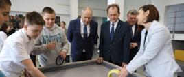 Minister Bernacki patrzy na dzieci puszczające kółka po szklanym stole.