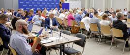 Grupa osób siedzi na sali przy stołach.