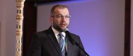 
Minister funduszy i polityki regionalnej Grzegorz Puda podczas spotkania z Konwentem Marszałków Województw RP, minister Puda stoi przy pulpicie i przemawia do mikrofonu