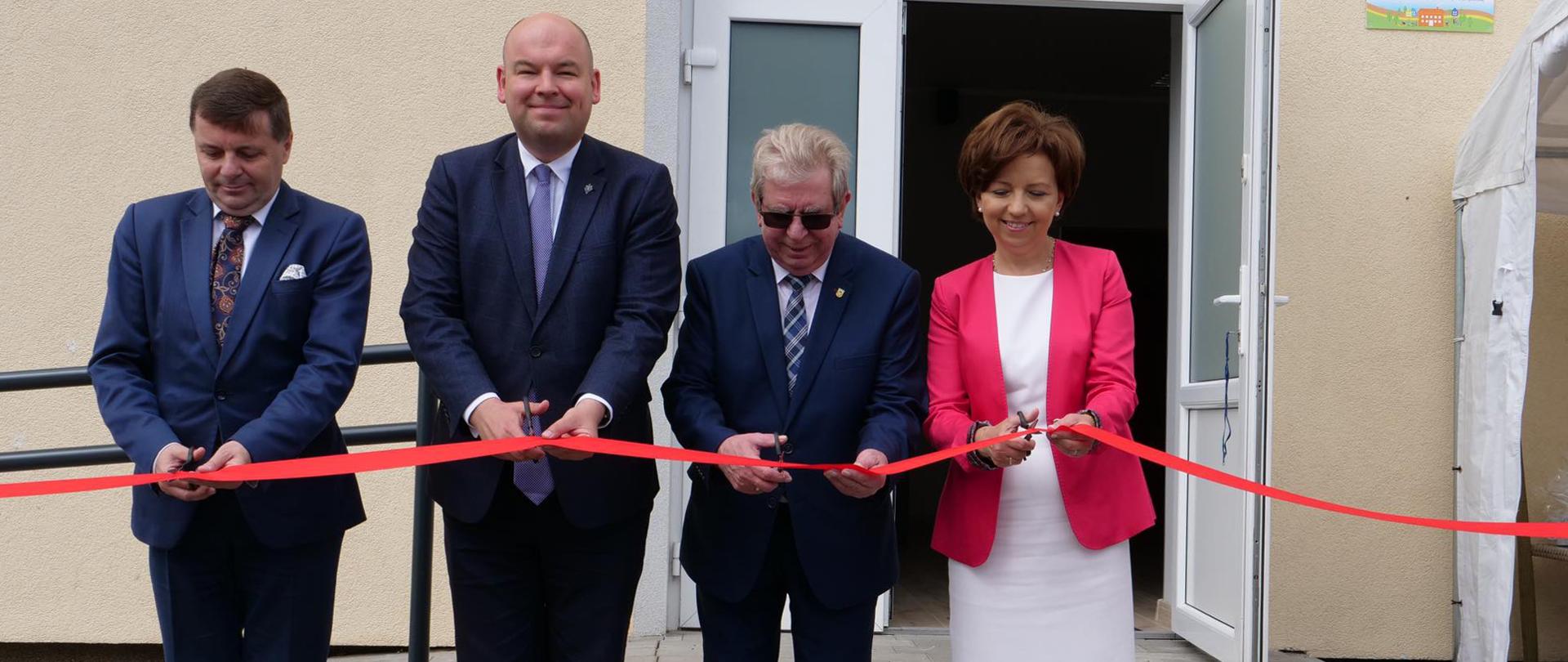 Osoby na pierwszym planie przecinają czerwoną wstęgę, oznaczającą otwarcie nowego klubu