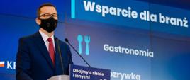 Premier Mateusz Morawiecki stoi podczas konferencji prasowej.