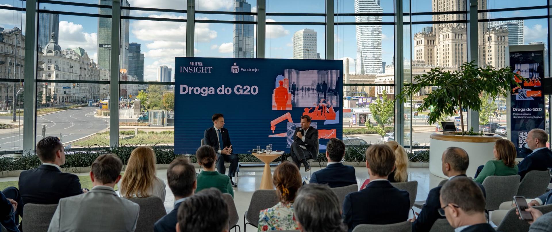 Uczestnicy siedzą na widowni podczas premiery raportu „Droga do G20. Polskie aspiracje i perspektywy członkostwa”. Na scenie trwa rozmowa, a w tle widoczna jest plansza z tytułem wydarzenia.