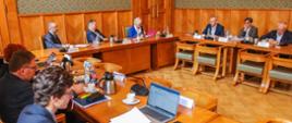 Widok z góry na salę, przy ustawionych w czworokąt stołach siedzi 9 osób.