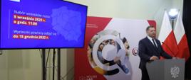 Minister Czarnek przemawia przy mikrofonie za nim ekran z prezentacją programu Poznaj Polskę 