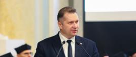 Minister Czarnek stoi i mówi do dwóch mikrofonów.