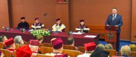 Widok z tyłu na salę, na krzesłach siedzą ceremonialnie ubrani ludzie, przed nimi przy mównicy stoi minister Czarnek i mówi do mikrofonu.