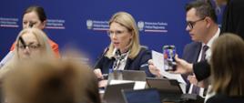 Na zdjęciu wiceminister Monika Sikora siedzi za stołem konferencyjnym w towarzystwie innych uczestników