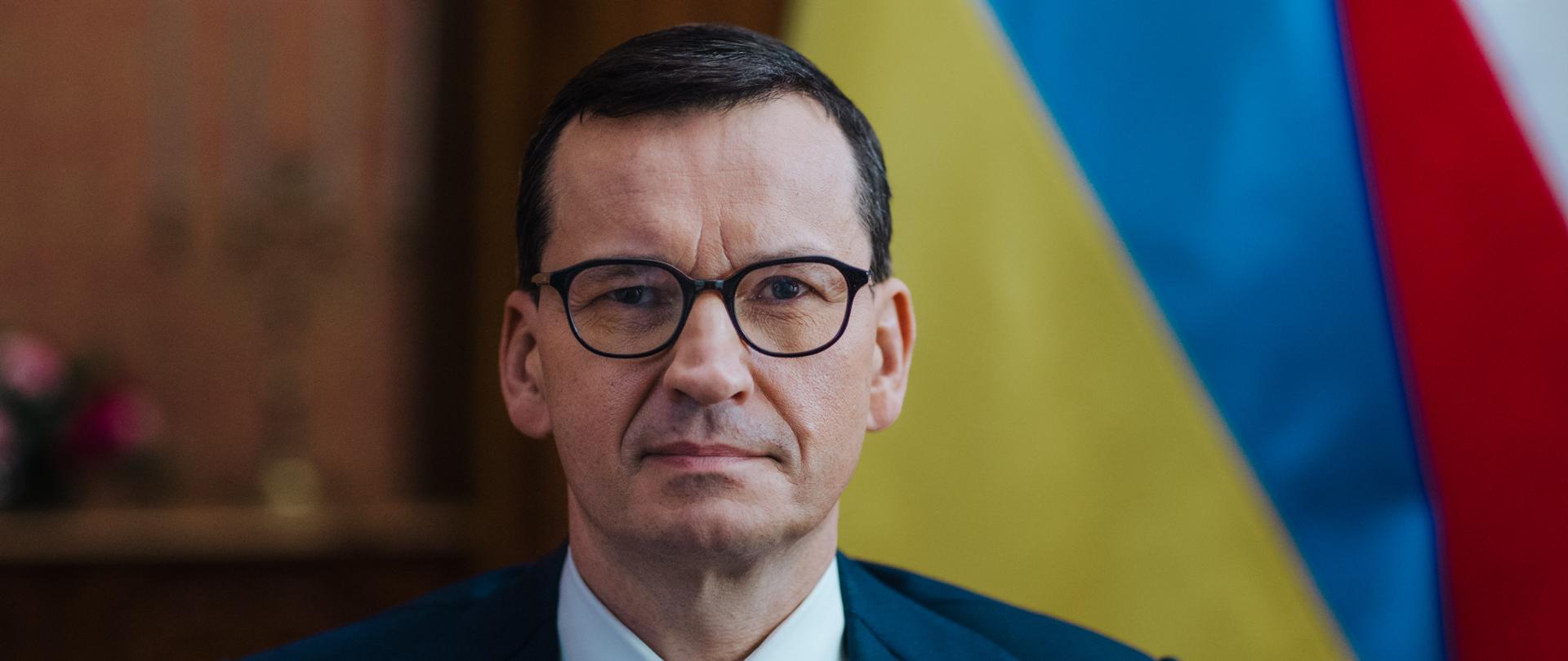 Premier Mateusz Morawiecki na flagach Polski i Ukrainy,