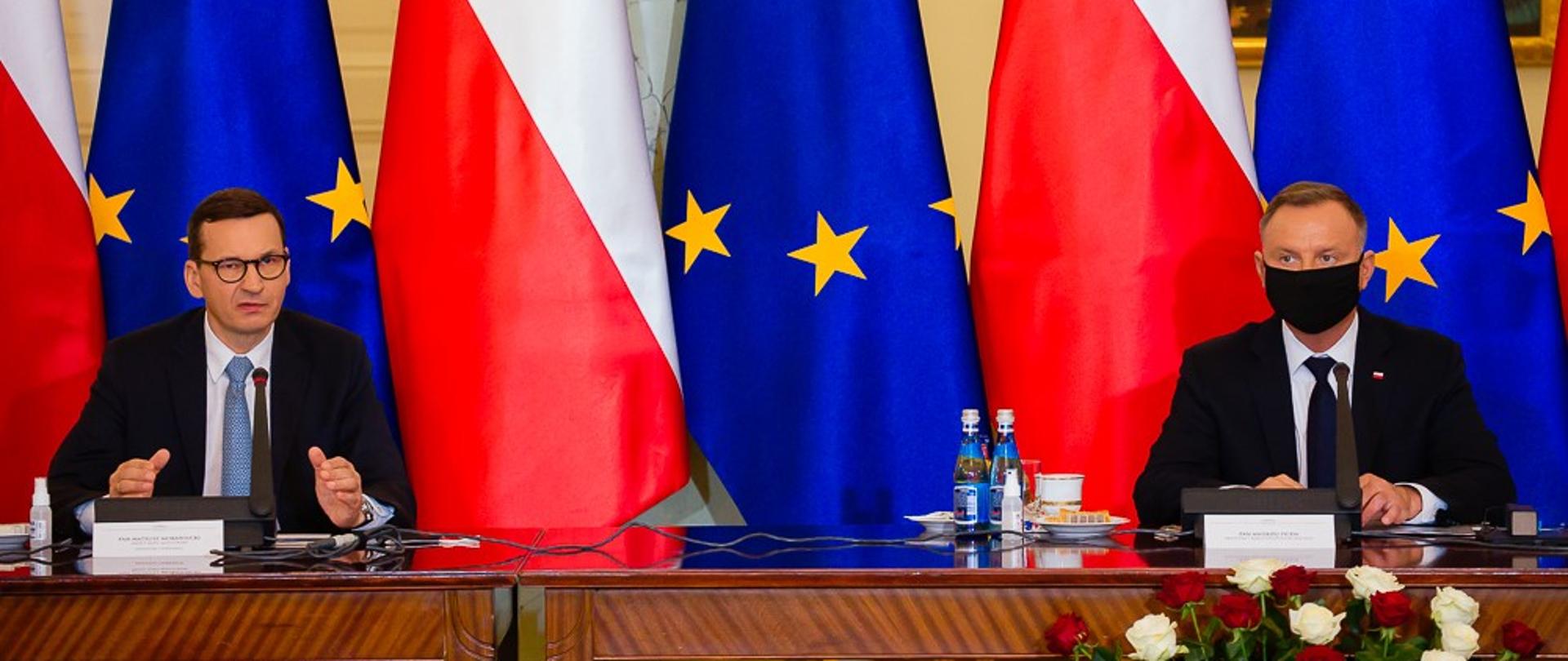 Premier Mateusz Morawiecki oraz prezydent Andrzej Duda siedzą przy stole. 