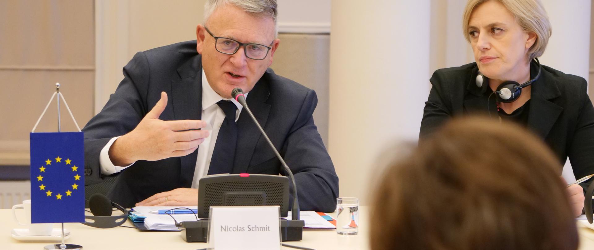 Spotkanie z komisarzem UE Nicolasem Schmitem. Zdjęcie ze spotkania w Ministerstwie. Na pierwszym planie Minister Marlena Maląg w nieostrosci, na drugim planie - komisarz oraz członek delegacji UE.