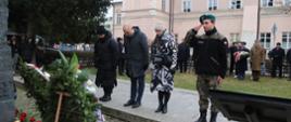 Przed czarnym pomnikiem stoją cztery osoby - dwie kobiety i mężczyzna w czarnej kurtce się kłaniają, młody chłopak w mundurze salutuje.