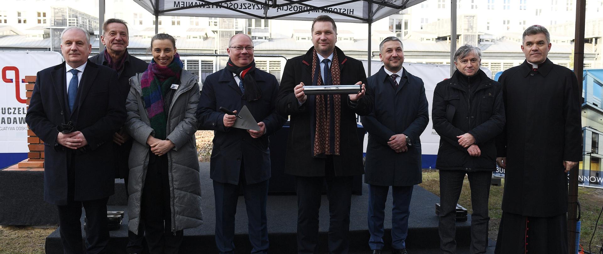 Wmurowanie kamienia węgielnego pod inwestycje Centrum Ekoinnowacji z udziałem ministra Przemysława Czarnka, minister Przemysław Czarnek stoi wśród innych uczestników ceremonii, w ręku trzyma kamień węgielny.