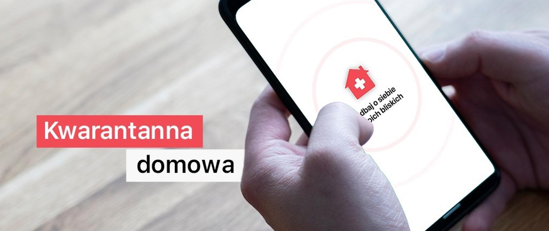 Dłonie trzymające smartfon. Na ekranie ikona i zakryty nieco napis -Zadbaj o siebie i swoich bliskich. Obok dłoni (po lewej stronie) napis kwarantanna domowa.