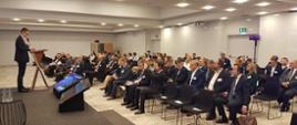 Sala konferencyjna. Wiceminister Karol Okoński przemawia do publiczności.