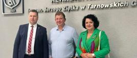 Minister stoi obok ubranej na zielono kobiety i mężczyzny w jasnej koszuli, za nimi na ścianie napis "REPTY" Górnośląskie Centrum Rehabilitacji.