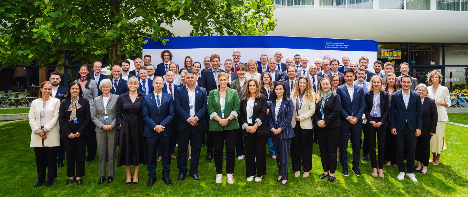 Spotkanie dyrektorów ds. sportu, zdjęcie grupowe na tle budynku oraz loga prezydencji