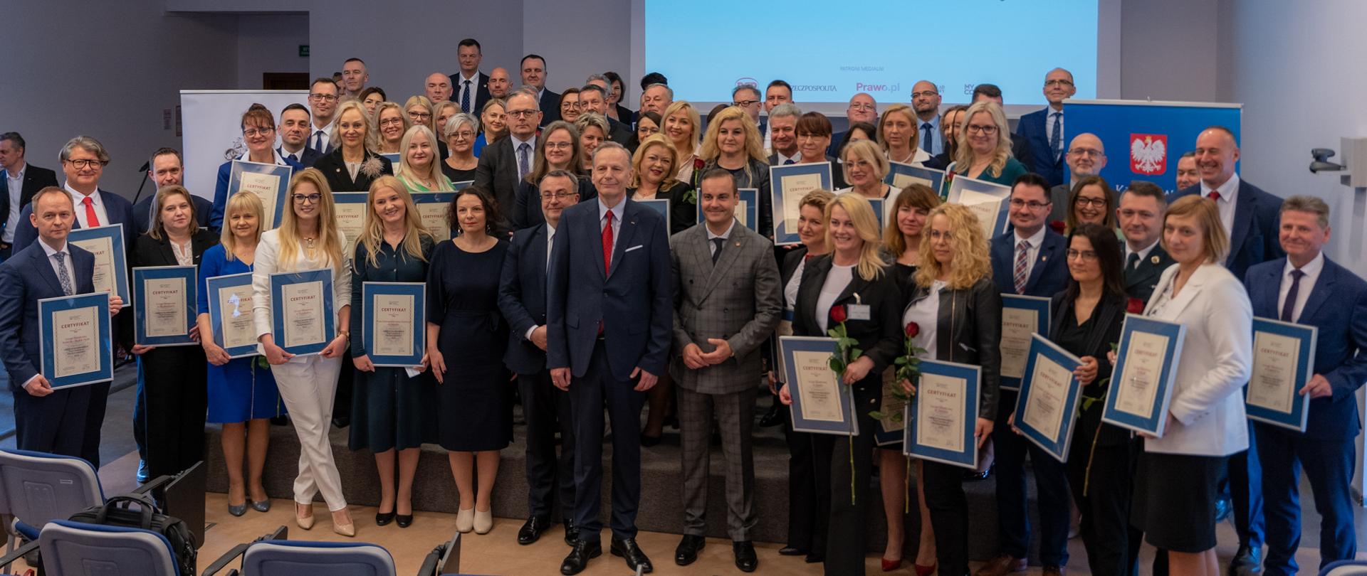 Szef KAS mł. insp. Bartosz Zbaraszczuk, prezes BCC Jacek Goliszewski, kierownictwo MF i przedstawiciele nagrodzonych Urzędów Skarbowych na tle banera Urząd Skarbowy Przyjazny Przedsiębiorcy