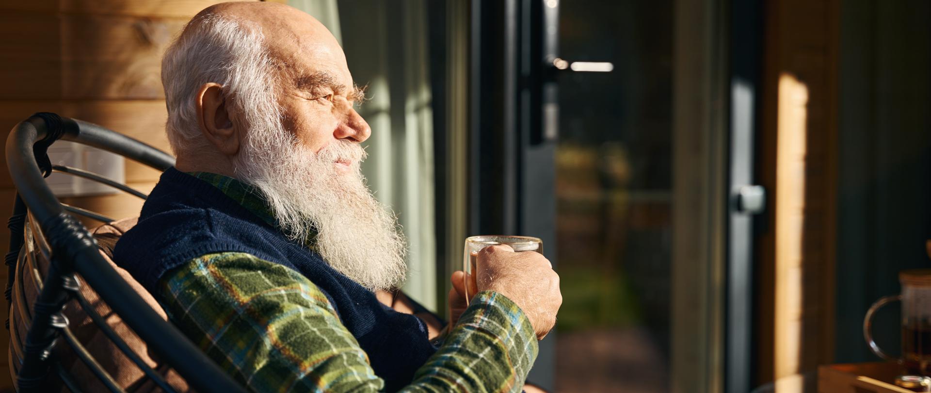 Elderly man is sitting on the veranda with a cup of tea, he is sitting in a comfortable chair