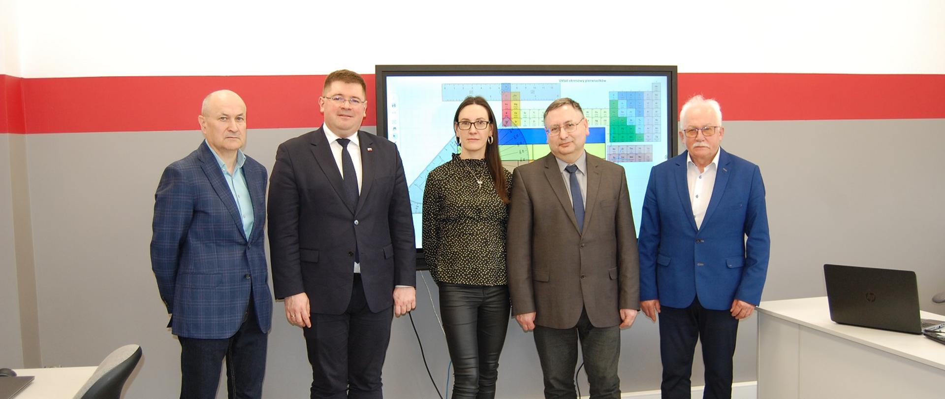 Wiceminister Tomasz Rzymkowski pozuje do zdjęcia w towarzystwie pracowników szkoły i władz samorządowych.
