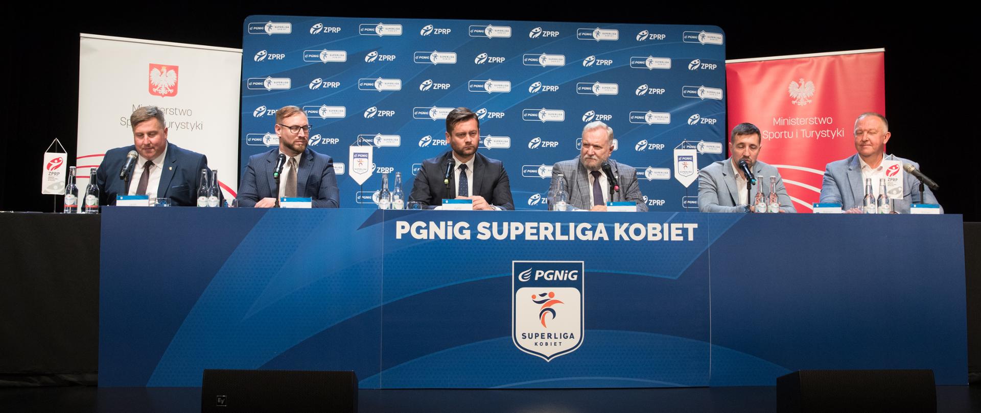 Konferencja prasowa ogłaszająca przystąpienie do Superligi Kobiet ukraińskiej drużyny Galychanki Lwów. Minister Kamil Bortniczuk oraz przedstawiciele Superligi i Związku Piłki Ręcznej w Polsce siedzą za stołem. Za nimi ścianki z logotypami, przed nimi napis PGNiG Superliga kobiet i logotyp Superligi kobiet.