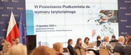 Grupa osób siedzi na sali przy stołach.