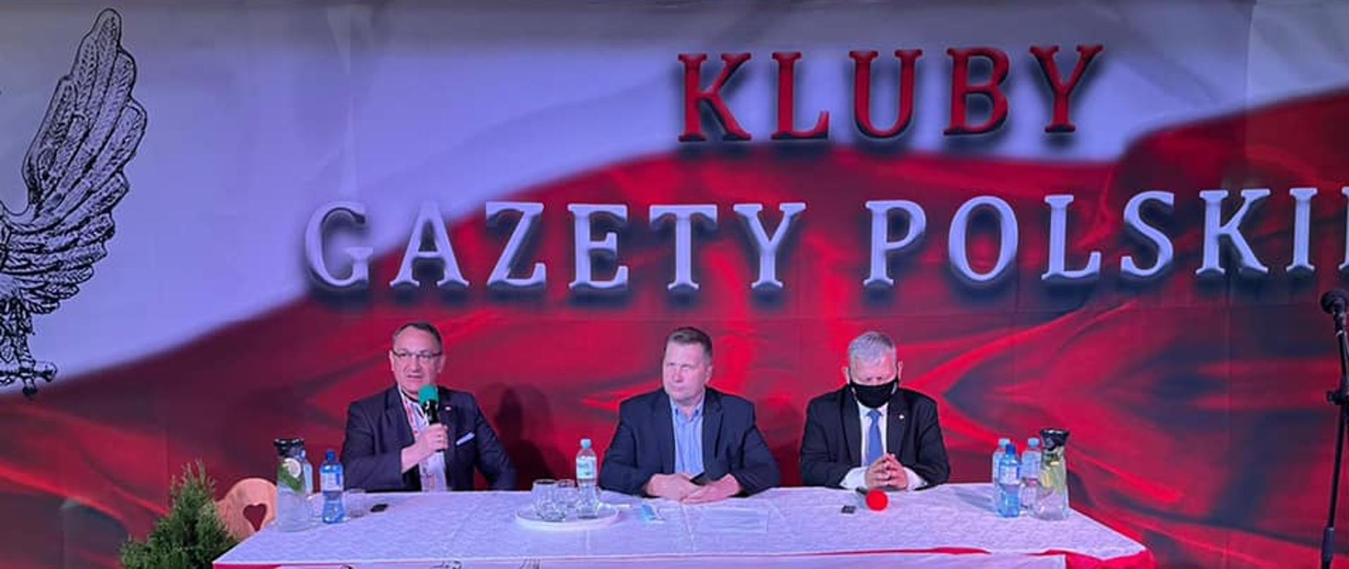 Minister Edukacji i Nauki Przemysław Czarnek siedzi przy stole obok dwóch prowadzących szesnasty Zjazd Klubów Gazety Polskiej.