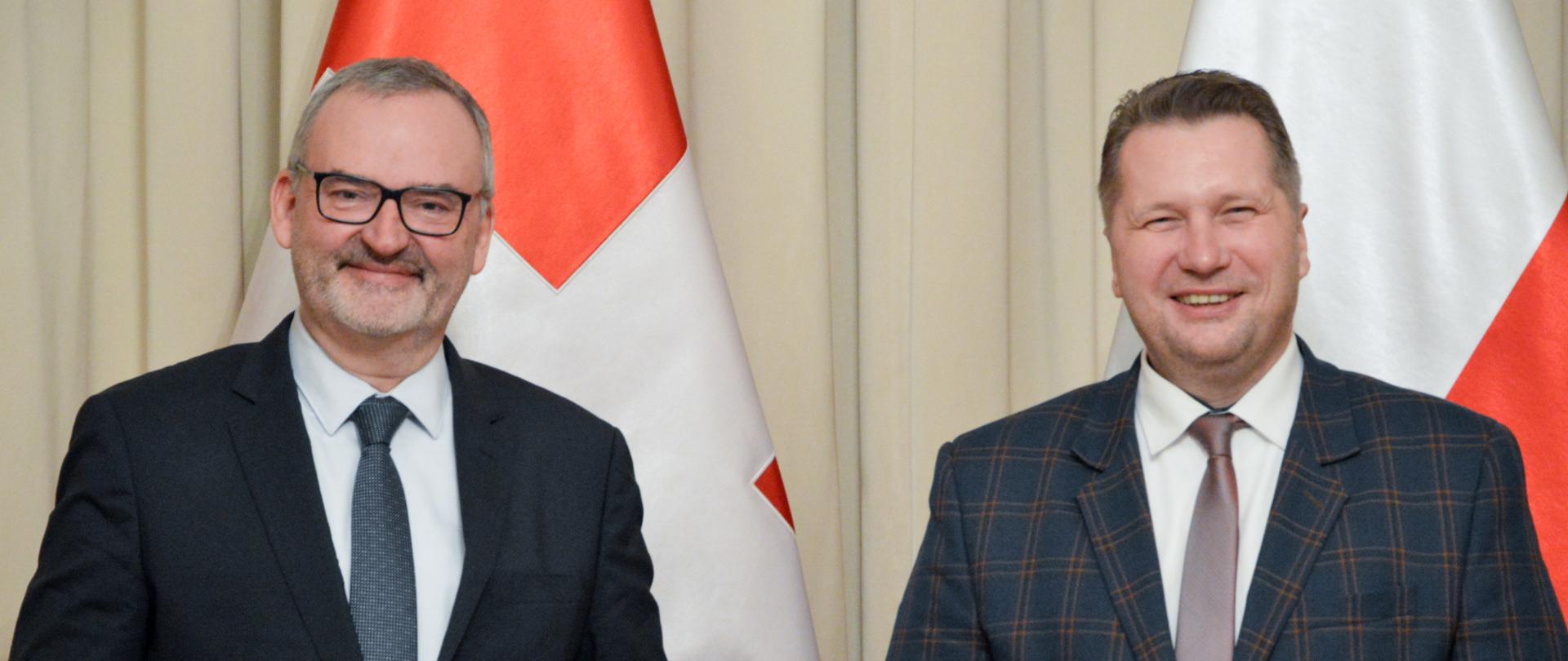 Minister Czarnek z Ambasadorem Szwajcarii za nimi flagi Polski