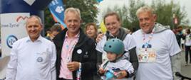 Pod nadmuchaną bramą stoi trzech mężczyzn i trzymająca małe dziecko w szarym rowerowym kasku kobieta.