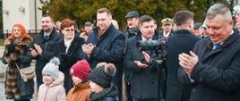 Zdjęcie na dworze, minister Czarnek stoi w dużej grupie ludzi, wszyscy klaszczą, z przodu stoi troje małych dzieci, z tyłu drzewo.