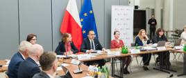 Pierwsze posiedzenie inauguracyjne Komitetu Monitorującego Krajowy Planu Odbudowy i Zwiększania Odporności - wiceminister funduszy i polityki regionalnej Marcin Horała siedzi przy stole i przemawia przez mikrofon, po jego lewej stronie siedzi dyrektor Departamentu Strategii w MFiPR Renata Calak