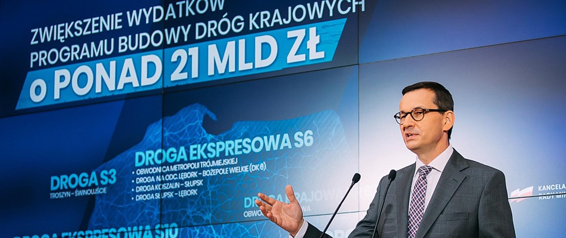Premier Mateusz Morawiecki na tle ścianki wizyjnej z mapą Polski.