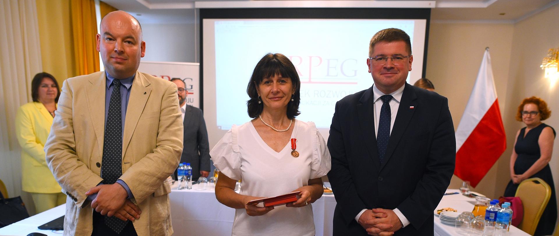 Mężczyzna w żółtej marynarce, kobieta w białej bluzce i minister Rzymkowski stoją obok siebie i patrzą w obiektyw.