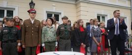 Pod jasnożółtą ścianą budynku stoi szereg harcerzy, z boku minister Czarnek bije brawo.