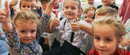Grupa małych dzieci. Śmieją się i pokazują kciuki w górę.