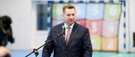 Minister Czarnek stoi przy mównicy z napisem Akademia Nauk Stosowanych i mówi do mikrofonu, za nim bramka piłkarska.