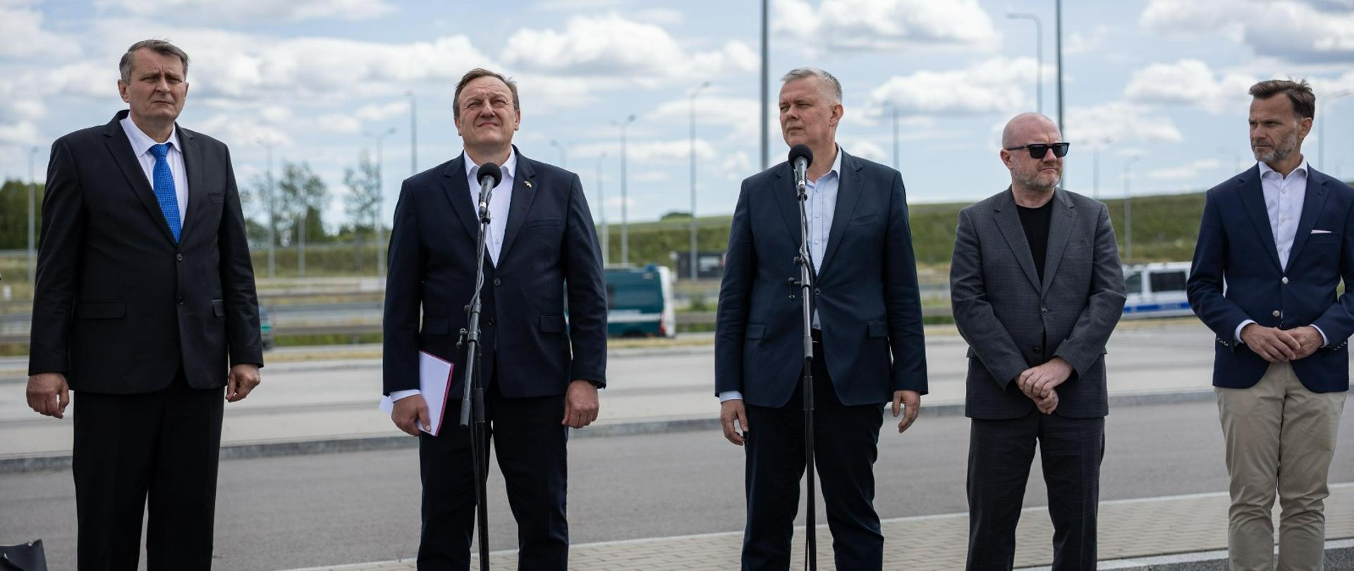 Minister Tomasz Siemoniak podczas spotkania z szefem MSW Litwy na przejściu granicznym w Budzisku. W tle samochody Straży Granicznej na drodze.
