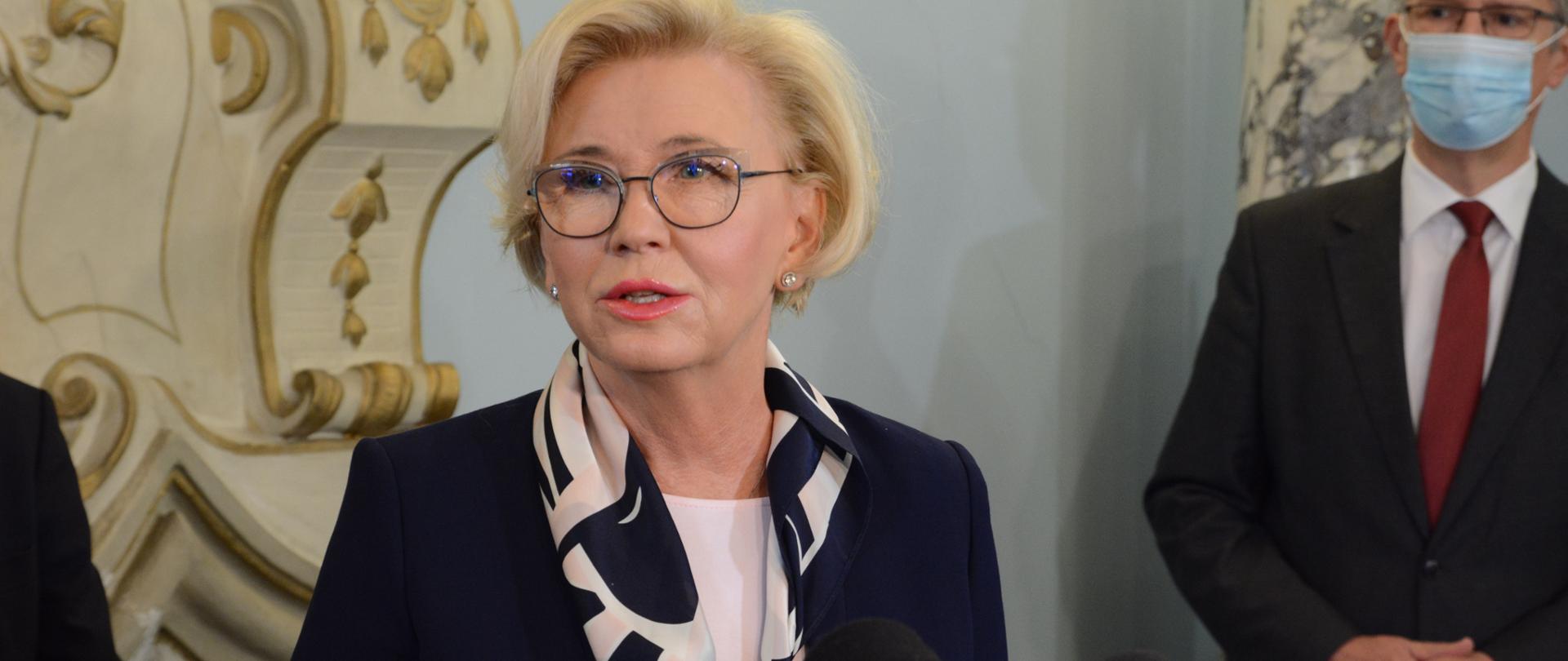 Wiceminister Marzena Machałek z wizytą w Zespole Szkół w Biedrzychowicach przemawia do mikrofonu, odpowiada na pytania dziennikarzy. 