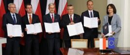 uczestnicy konferencji trzymają otwarte umowy o dofinansowanie z funduszy unijnych