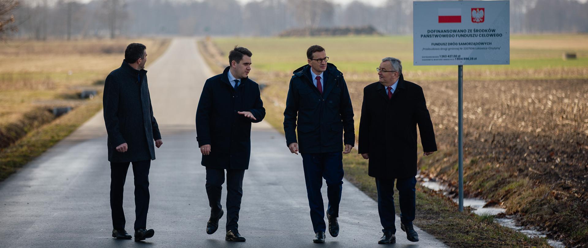 Premier, minister infrastruktury oraz poseł Daniel Milewski idą na tle drogi.