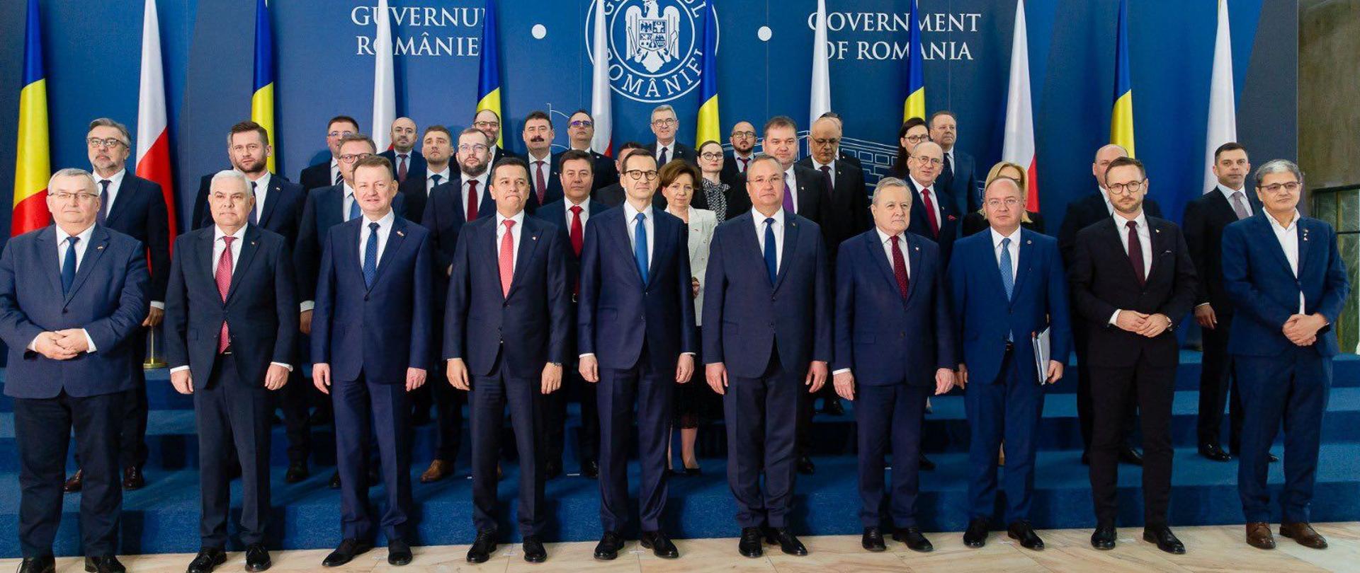 Duża grupa mężczyzn w garniturach stoi pod niebieską ścianą.