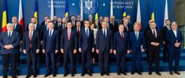 Duża grupa mężczyzn w garniturach stoi pod niebieską ścianą.
