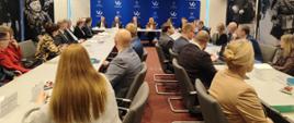 W sali konferencyjnej odbywa się spotkanie ministry klimatu i środowiska Pauliny Hennig-Kloski z przedstawicielami i przedstawicielkami Wód Polskich, Urzędu Marszałkowskiego, samorządów i ZE PAK S.A. Uczestnicy słuchają wypowiedzi gości.