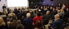 Sala konferencyjna na której siedzą na krzesłach samorządowcy, pod ekranem stół za którym siedzi minister funduszy i polityki regionalnej Katarzyna Pełczyńska-Nałęcz i dyrektorzy MFiPR