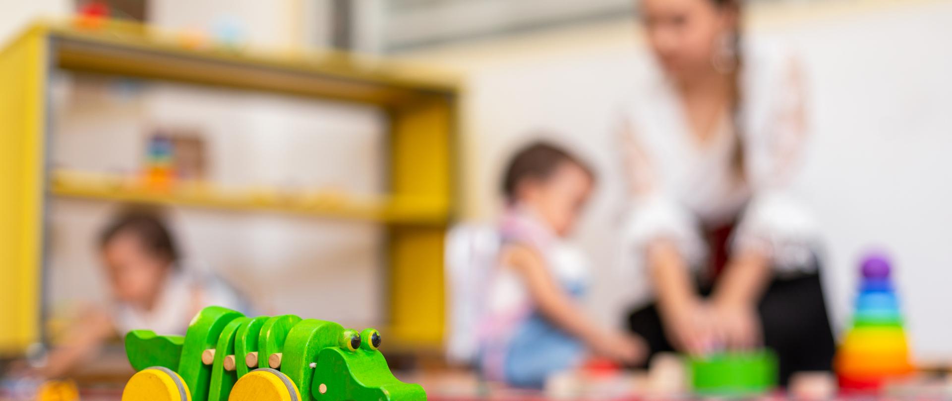Closeup of wooden crocodile toy and kids playing with toys in the background in kindergarten