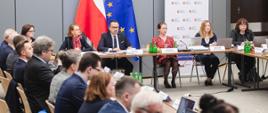 Pierwsze posiedzenie Komitetu Monitorującego Krajowy Plan Odbudowy - wiceminister funduszy i polityki regionalnej Marcin Horała siedzi przy stole i przemawia przez mikrofon, po jego lewej stronie siedzi dyrektor Departamentu Strategii w MFiPR Renata Calak