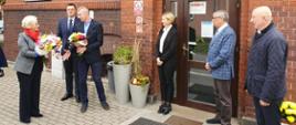 Wiceminister Marzena Machałek z wizytą w Zgorzelcu, wiceminister Marzena Machałek otrzymuje kwiaty od społeczności Ośrodka Szkolno-Wychowawczego w Zgorzelcu, stoi razem z pracownikami na tle budynku placówki
