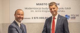 Wiceminister Piontkowski ściska rękę mężczyzny w garniturze, za nimi na ścianie tablica z napisem Miasto Brańsk.