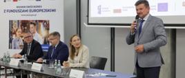 Minister funduszy i polityki regionalnej Katarzyna Pełczyńska-Nałęcz na spotkaniu z przedsiębiorcami woj. opolskiego, minister siedzi przy stole, po jej lewej stronie stoi i przemawia do mikrofonu wicewojewoda opolski Piotr Pośpiech