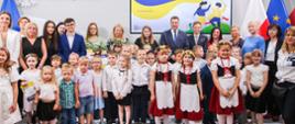 Zdjęcie zbiorowe, duża grupa dzieci stoi pod ścianą, na której jest napis Dobry obywatel.