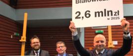 Wiceminister klimatu i środowiska Mikołaj Dorożała podczas wizyty w Białowieskim Parku Narodowym. Na zdjęciu wiceminister trzyma plansze z wysokością subwencji dla Białowieży. 